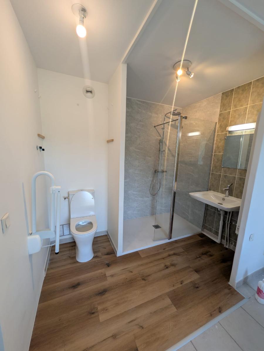 Salle de bains PMR : douche de plain-pied, lavabo accessible et WC avec barre d'appui relevable